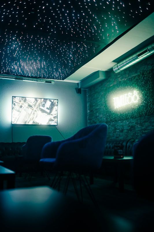 Lounge mit Sesseln, Screen und Timeless-Neonschild